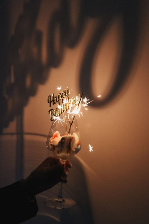 Vela de aniversário acesa com faíscas e a palavra 'Parabéns!' em destaque, festa e celebração Maria Madame Cestas.