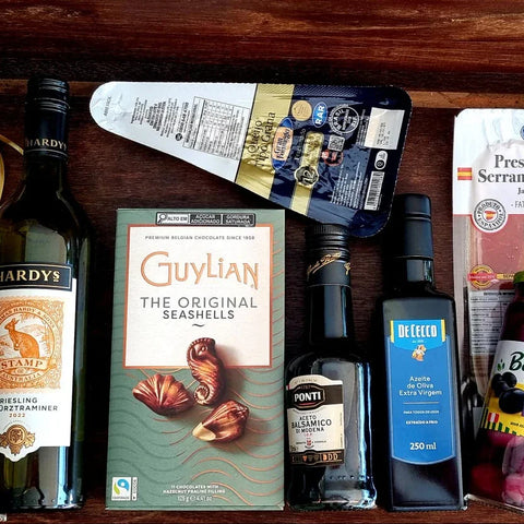 Cesta gourmet com vinho, chocolates Guylian, azeite, balsâmico, queijo e presunto cru.