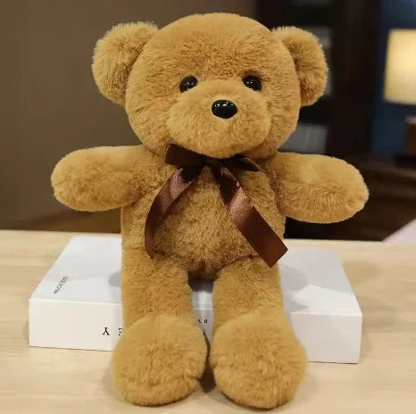 Ursinho de pelúcia marrom com laço de fita em mesa, ideal para cestas de presente Maria Madame.